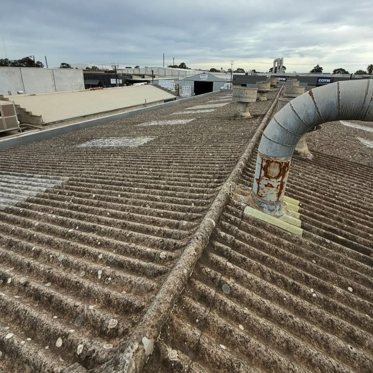 Weathered old asbestos roof sheets on a commercial building, with a rusted flue
