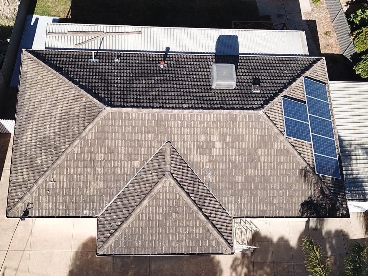 Old tiled hip roof from above, with a small solar array and an evaporative cooler